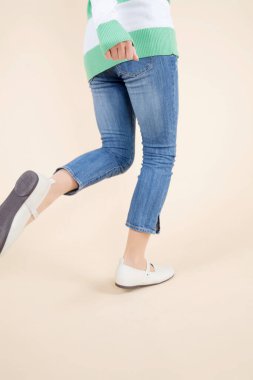 Stüdyoda kot pantolon ve çizgili kazakla yürüyen genç bir kadın.