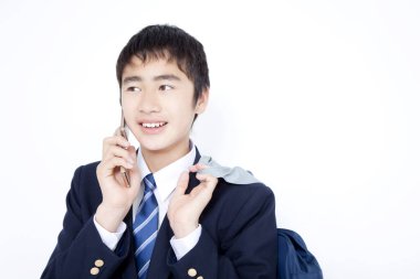 Asyalı okul üniformalı çocuk beyaz arka planda izole bir şekilde cep telefonuyla konuşuyor.