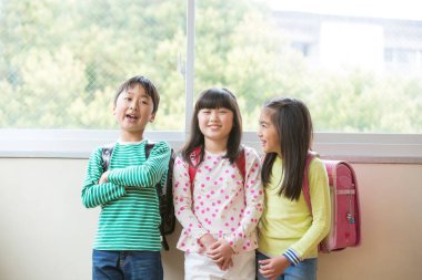 Okul koridorunda sırt çantalı bir grup Asyalı öğrenci.