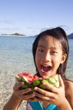 Deniz kıyısında karpuz yiyen Asyalı küçük kız