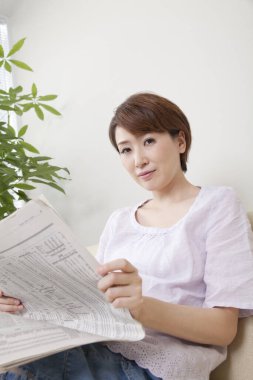 Asyalı kadın evde gazete okuyor.