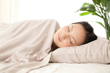 Güzel genç Asyalı kadın evde yatakta uyuyor. 