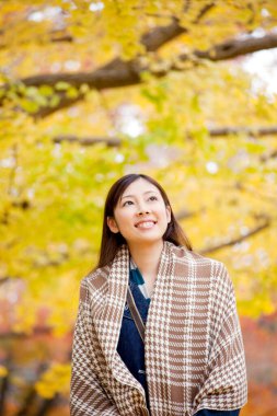Güzel Asyalı kadın sonbahar parkında geziniyor.