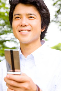 Asyalı genç adam dışarıda cep telefonu kullanıyor.