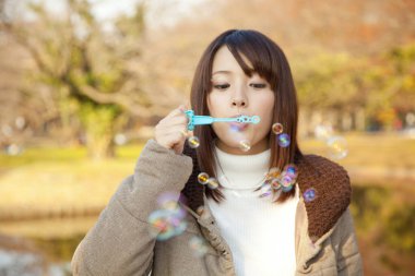 Genç Asyalı kadın sonbahar parkında baloncuk çıkarıyor. 