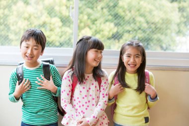 Okul koridorunda sırt çantalı bir grup Asyalı öğrenci.