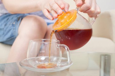 Genç bir kadın cam kaseye çay dolduruyor. 