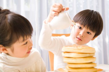 Küçük çocuk kreplere bal döküyor. 