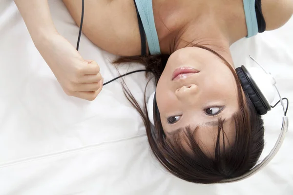美しい若いアジアの女性はベッドに横たわり 自宅でヘッドフォンで音楽を聞いています — ストック写真