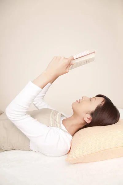 Lächelnde Asiatin Liest Buch Während Sie Auf Einem Bett Liegt — Stockfoto