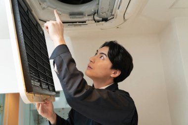 Genç Asyalı adam evdeki havalandırmayı tamir ediyor..