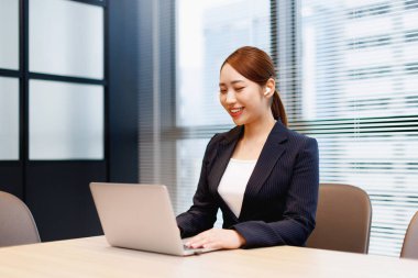 Modern ofis binasında dizüstü bilgisayarda çalışan güzel bir Japon kadın.