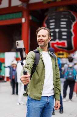 Yeşil tişörtlü genç beyaz adam cep telefonuyla selfie çekiyor.