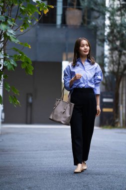 Genç Asyalı iş kadını şehir caddesinde yürüyor.