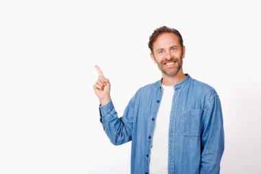 Beyaz stüdyo arkaplanını işaret eden mavi gömlekli beyaz bir adamın portresi.