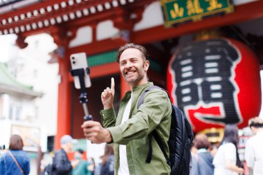 Yeşil tişörtlü genç beyaz adam cep telefonuyla selfie çekiyor.