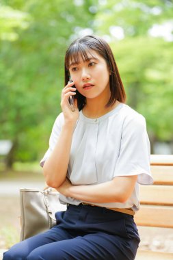 Düşünceli genç Asyalı kadın yaz parkında akıllı telefondan konuşuyor.