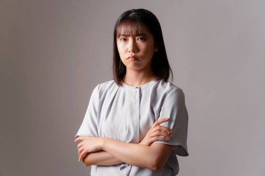 Kollarını kavuşturup kameraya bakan Asyalı genç bir kadın. 