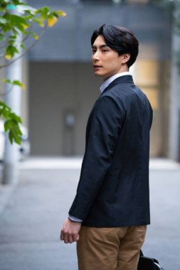 Takım elbiseli yakışıklı Asyalı genç işadamının portresi. Şehir caddesinde yürüyor. 