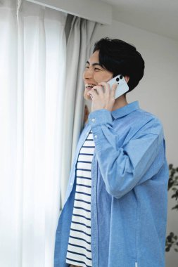 Genç ve yakışıklı adam evde akıllı telefon kullanarak kendine güveniyor.