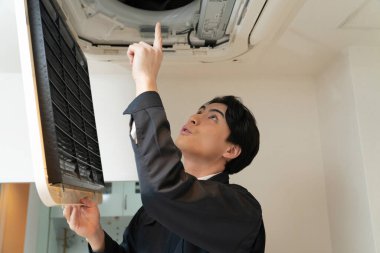 Genç Asyalı adam evdeki havalandırmayı tamir ediyor..