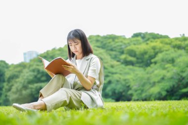 Yaz parkında kitap okuyan Asyalı genç bir kadın..