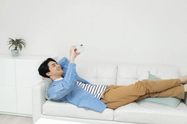 Evdeki kanepede akıllı telefonlu genç Asyalı adam..