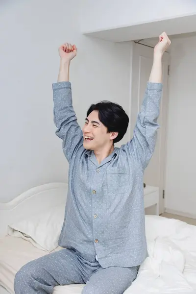 handsome asian man wearing pajamas stretching after sleep