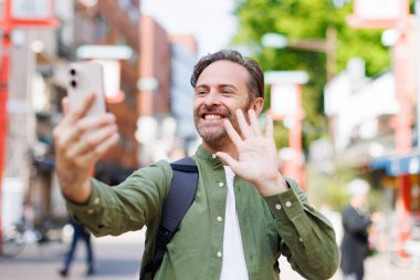 Yeşil tişörtlü genç beyaz adam cep telefonuyla selfie çekiyor. 