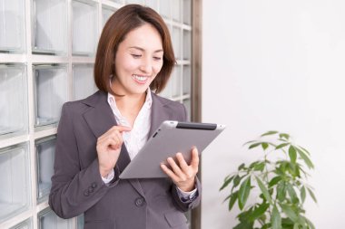 Ofiste tablet kullanan takım elbiseli Japon iş kadını.
