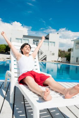 Asyalı adam yüzme havuzunun yanında dinleniyor.