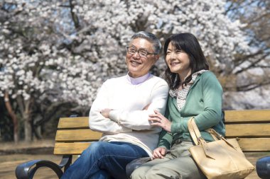 Güzel Asyalı olgun çift çiçek açan kiraz ağaçlarına karşı poz veriyor.