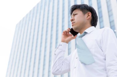 Asyalı işadamı şehirde akıllı telefon kullanıyor.