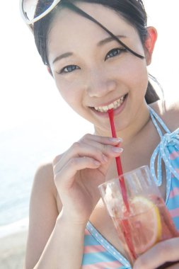 Bikinili bir kadın sahilde içki içiyor. 