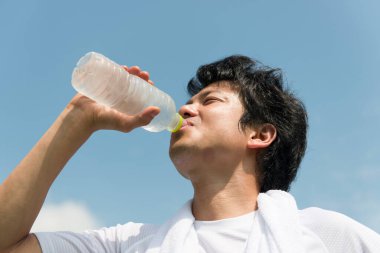 Genç Asyalı adam egzersizden sonra şişeden su içiyor.