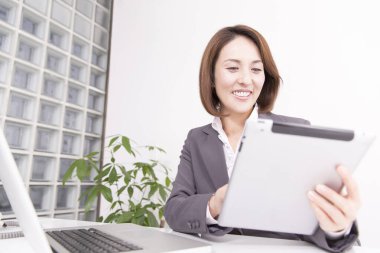 Ofiste tablet kullanan takım elbiseli Japon iş kadını.