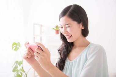 Asyalı genç kadın evde akıllı telefon kullanıyor.