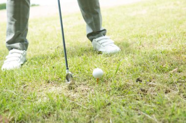 Beyaz gömlekli ve gri pantolonlu bir Asyalı golf oynuyor.