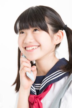 Okul üniformalı, beyaz arka planda cep telefonu olan güzel bir öğrencinin portresi.