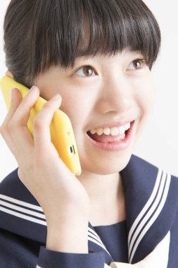 Okul üniformalı genç Asyalı kızın portresi akıllı telefondan konuşuyor.