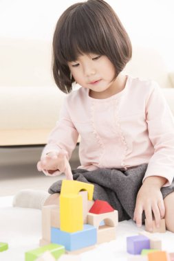 Küçük sevimli Asyalı kız tahta oyuncak bloklarıyla oynuyor.