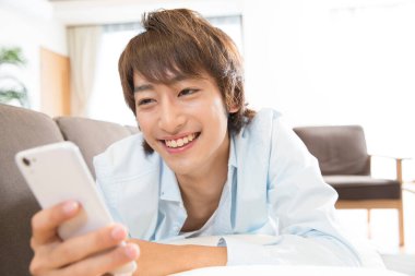 Genç Asyalı adam gülümsüyor ve akıllı telefon kullanıyor. 