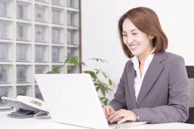 Ofiste dizüstü bilgisayarla çalışan takım elbiseli Japon iş kadını.