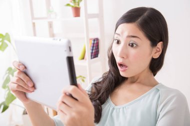 Evde tablet kullanan şok olmuş bir kadın.