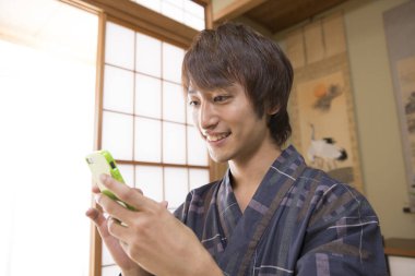 Geleneksel Yukata 'daki yakışıklı Japon genç adamın portresi. Etnik kaplıca otelinde akıllı telefon kullanıyor.
