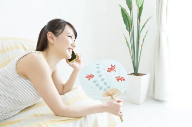 Kadın telefon kullanıyor ve vantilatör tutuyor. 