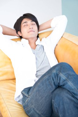 Genç Asyalı adam kanepede dinleniyor.