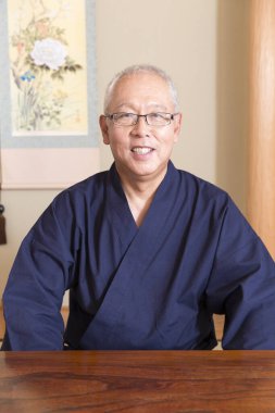 Masada oturan gülümseyen Japon kıdemli adam. 