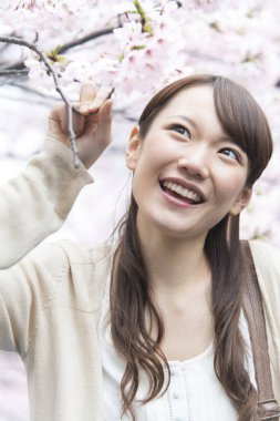 Ağaçların önünde pembe çiçekli genç bir kadın.