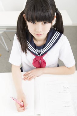 Okul üniformalı gülümseyen Japon öğrenci okulda ders çalışıyor.